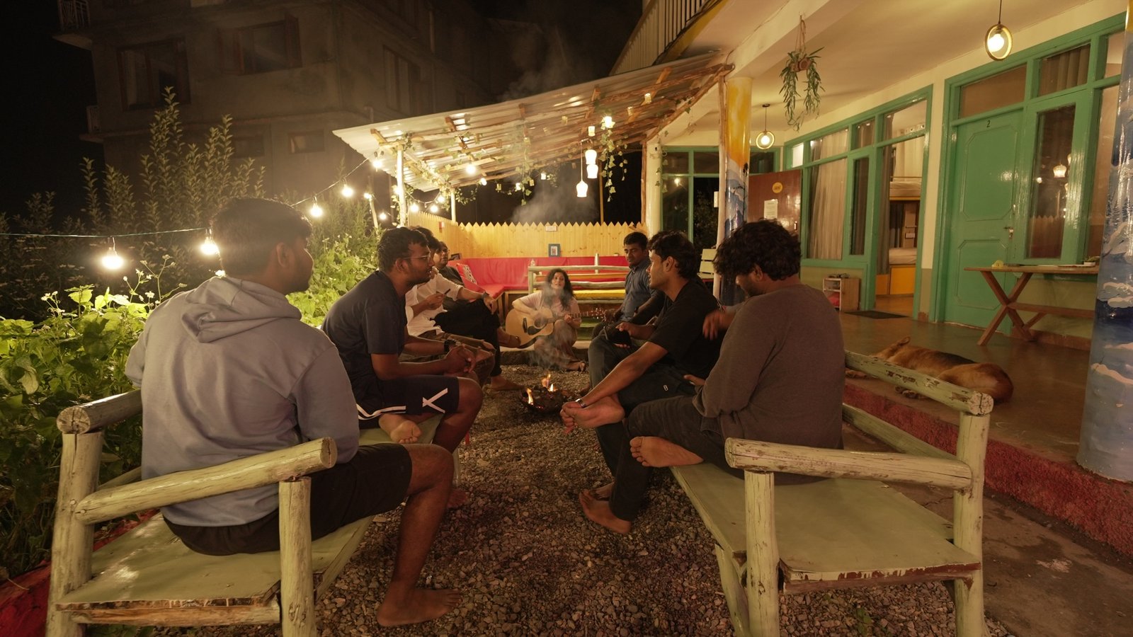 Travellers around a Safar terrace bonfire while a guest plays guitar